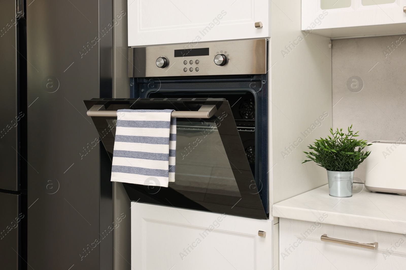 Photo of Open electric oven with striped towel in kitchen. Cooking appliance