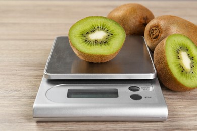 Photo of Kitchen scale with piece of kiwi on light wooden table, closeup