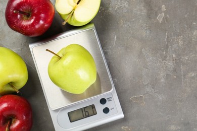 Photo of Kitchen scale with apple among ones on grey textured table, flat lay. Space for text