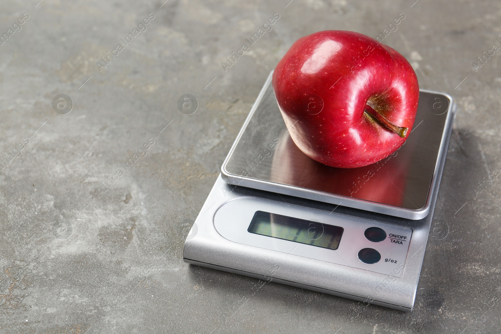 Photo of Kitchen scale with apple on grey textured table, closeup. Space for text