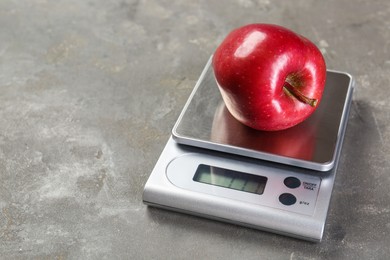 Photo of Kitchen scale with apple on grey textured table, closeup. Space for text