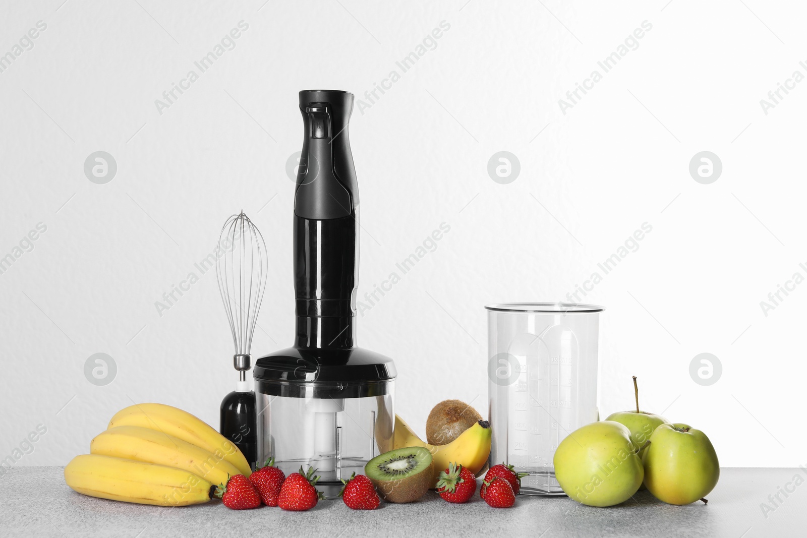 Photo of Hand blender kit, fresh fruits and strawberries on gray table against white background