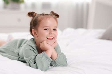 Photo of Portrait of happy little girl on bed at home, space for text