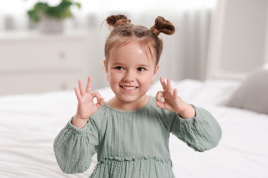 Photo of Portrait of happy little girl showing OK gesture in bedroom