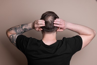 Photo of Baldness concept. Man with bald spot on beige background, back view