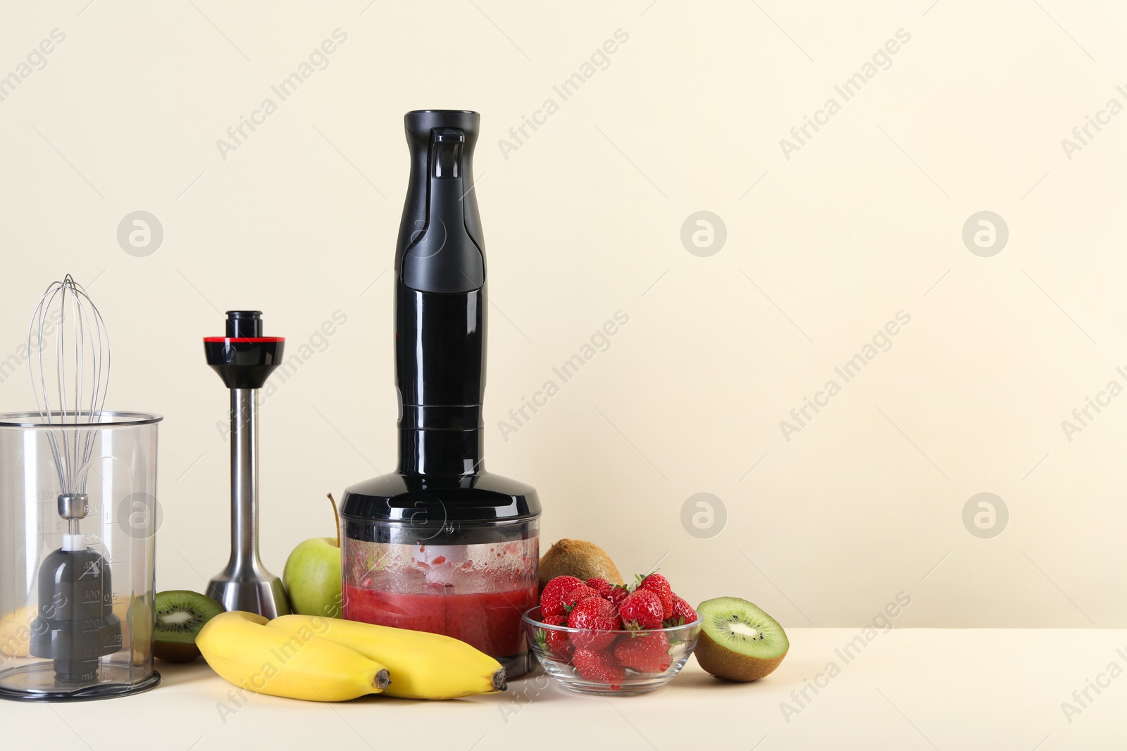 Photo of Hand blender kit, mixture of ingredients and fresh fruits on beige background, space for text