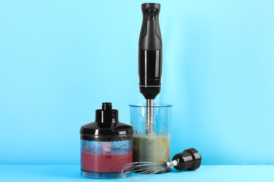 Photo of Hand blender kit and mixtures of ingredients on light blue background