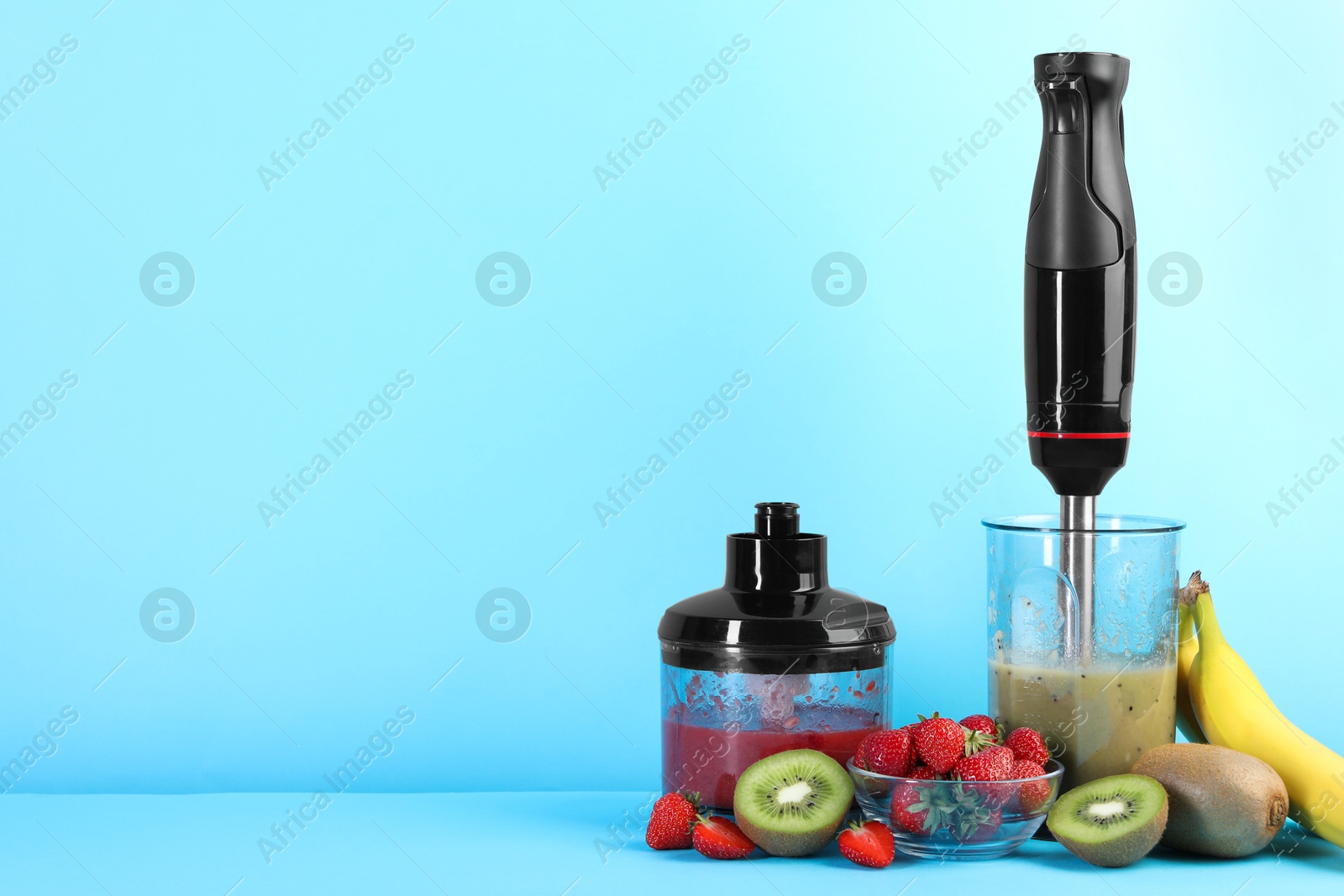 Photo of Hand blender kit, mixtures of ingredients and fresh fruits on light blue background, space for text