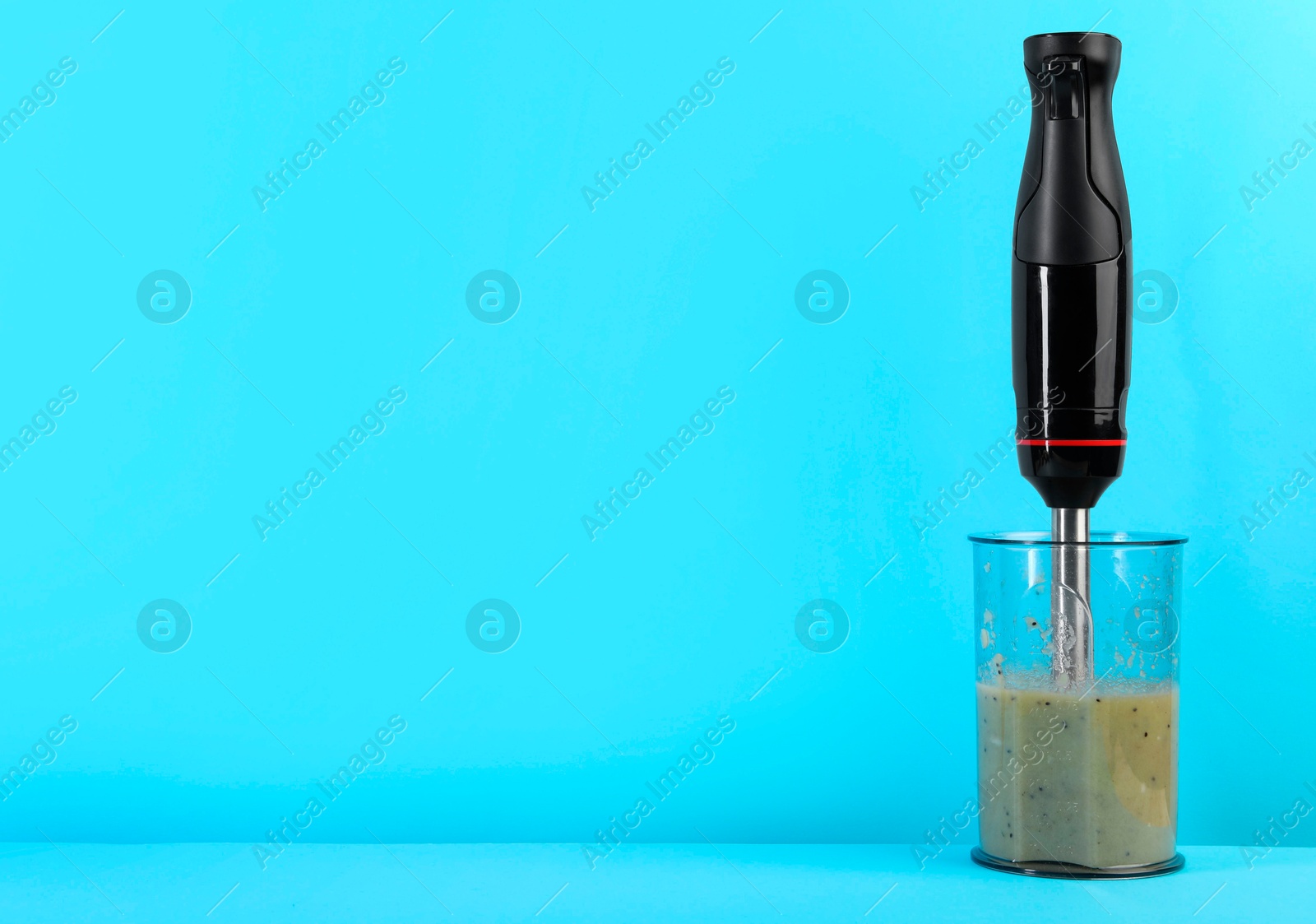 Photo of Hand blender with mixture of ingredients on light blue background, space for text