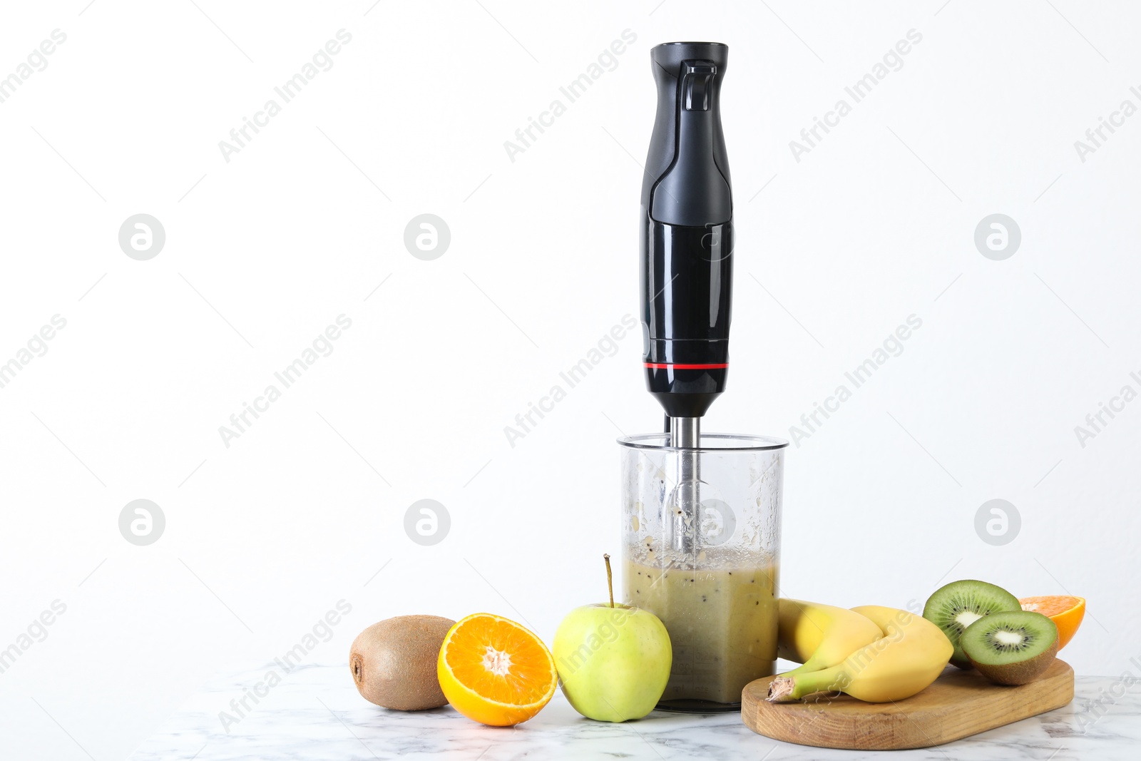 Photo of Hand blender with mixture of ingredients and fresh fruits on white marble table, space for text