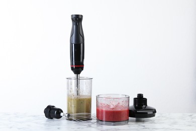 Photo of Hand blender kit and mixtures of ingredients on white marble table