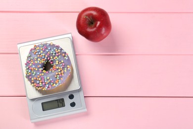 Photo of Kitchen scale with donut and apple on pink wooden table, top view. Space for text