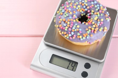 Photo of Kitchen scale with donut on pink wooden table, space for text