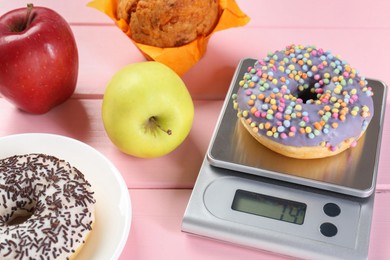 Kitchen scale with donut and other products on pink wooden table