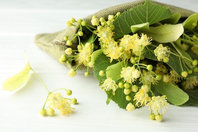 Fresh linden leaves and flowers on white wooden table, closeup