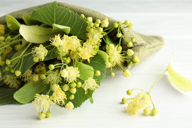 Fresh linden leaves and flowers on white wooden table, closeup