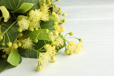 Photo of Fresh linden leaves and flowers on white wooden table, closeup. Space for text