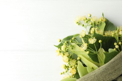 Fresh linden leaves and flowers in bag on white wooden table, top view. Space for text