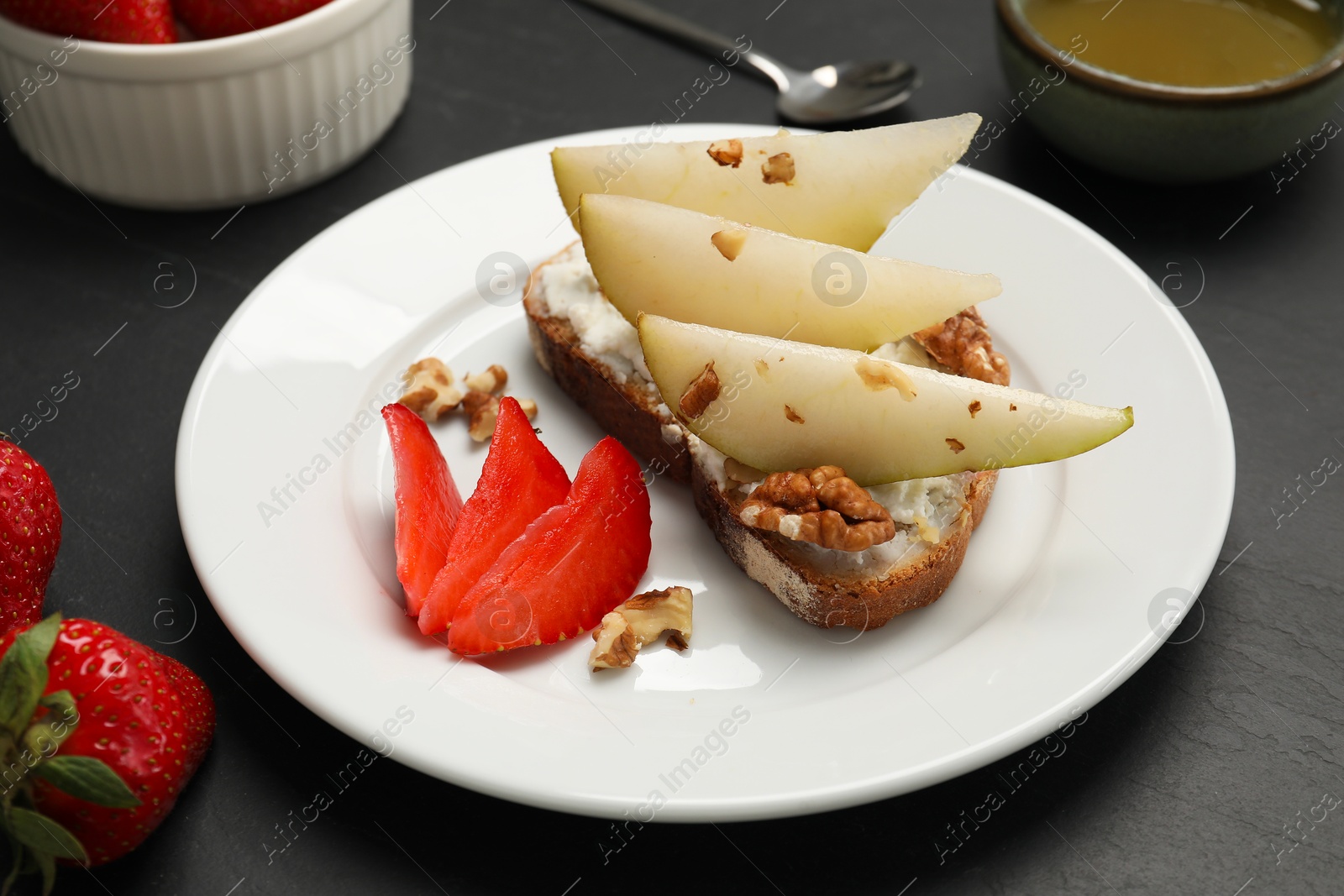 Photo of Delicious ricotta bruschetta with pear, strawberry and walnut on black table