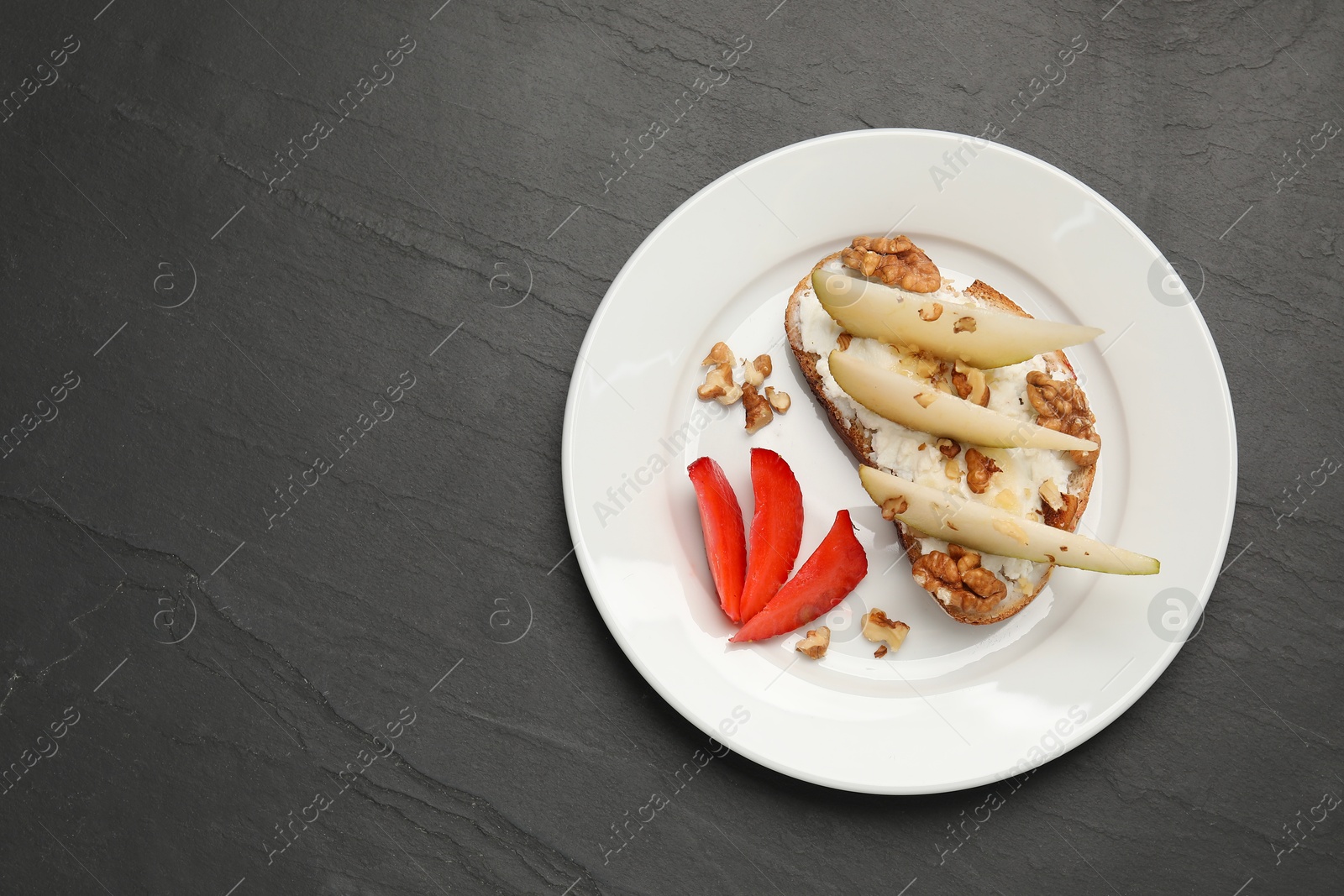 Photo of Delicious ricotta bruschetta with pear, strawberry and walnut on black table, top view. Space for text