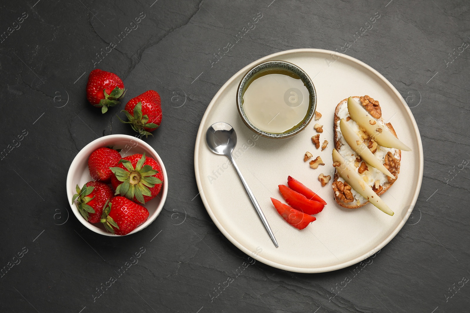 Photo of Delicious ricotta bruschetta with pear, strawberry and walnut on black table, flat lay