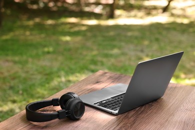 Photo of Laptop and headphones on wooden table outdoors. Remote work