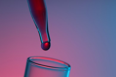 Dripping liquid from pipette into test tube on color background, closeup. Space for text