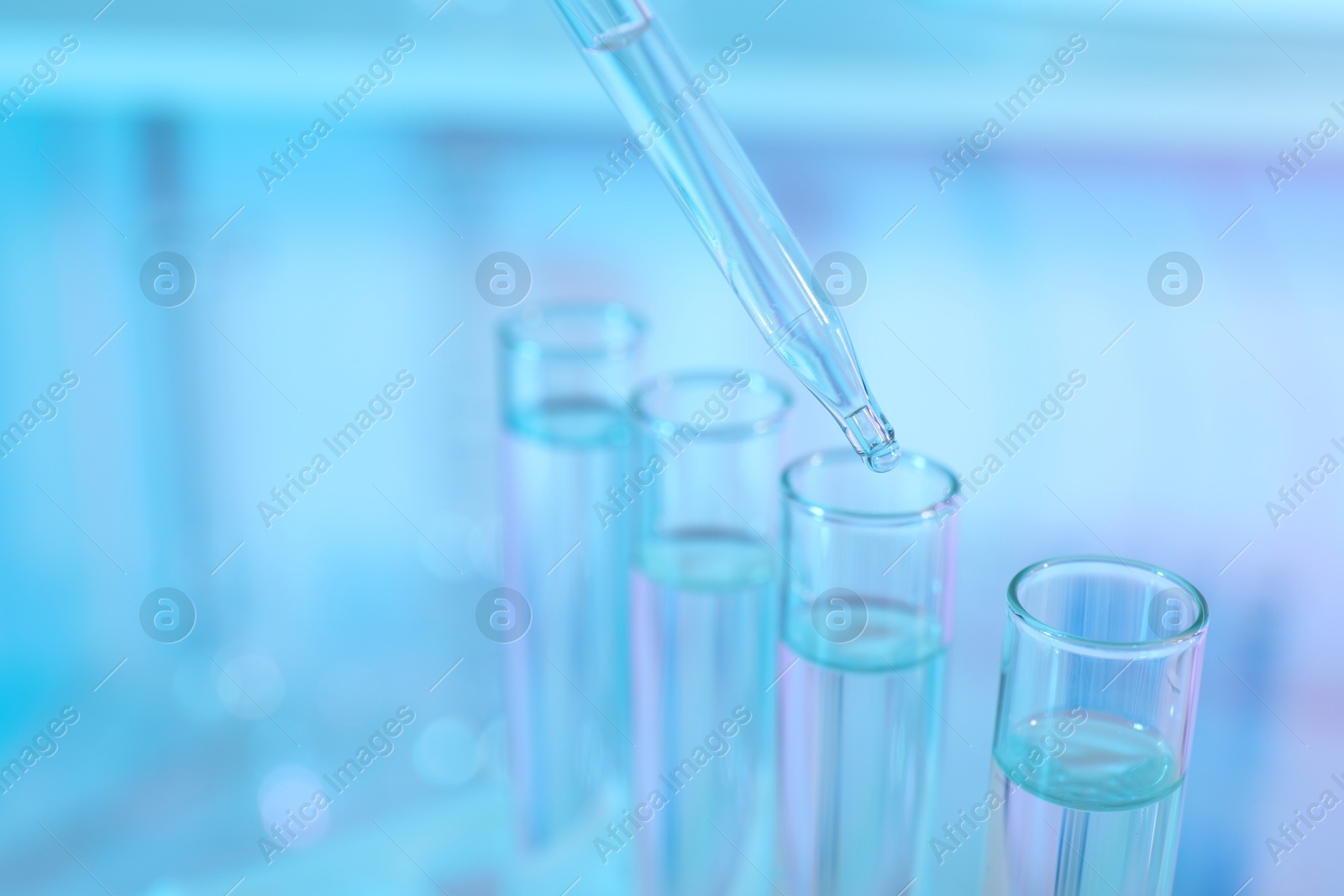 Photo of Dripping liquid from pipette into test tube on light blue background, closeup