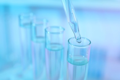 Photo of Dripping liquid from pipette into test tube on light blue background, closeup