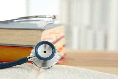 Photo of One new medical stethoscope and books on wooden table, closeup