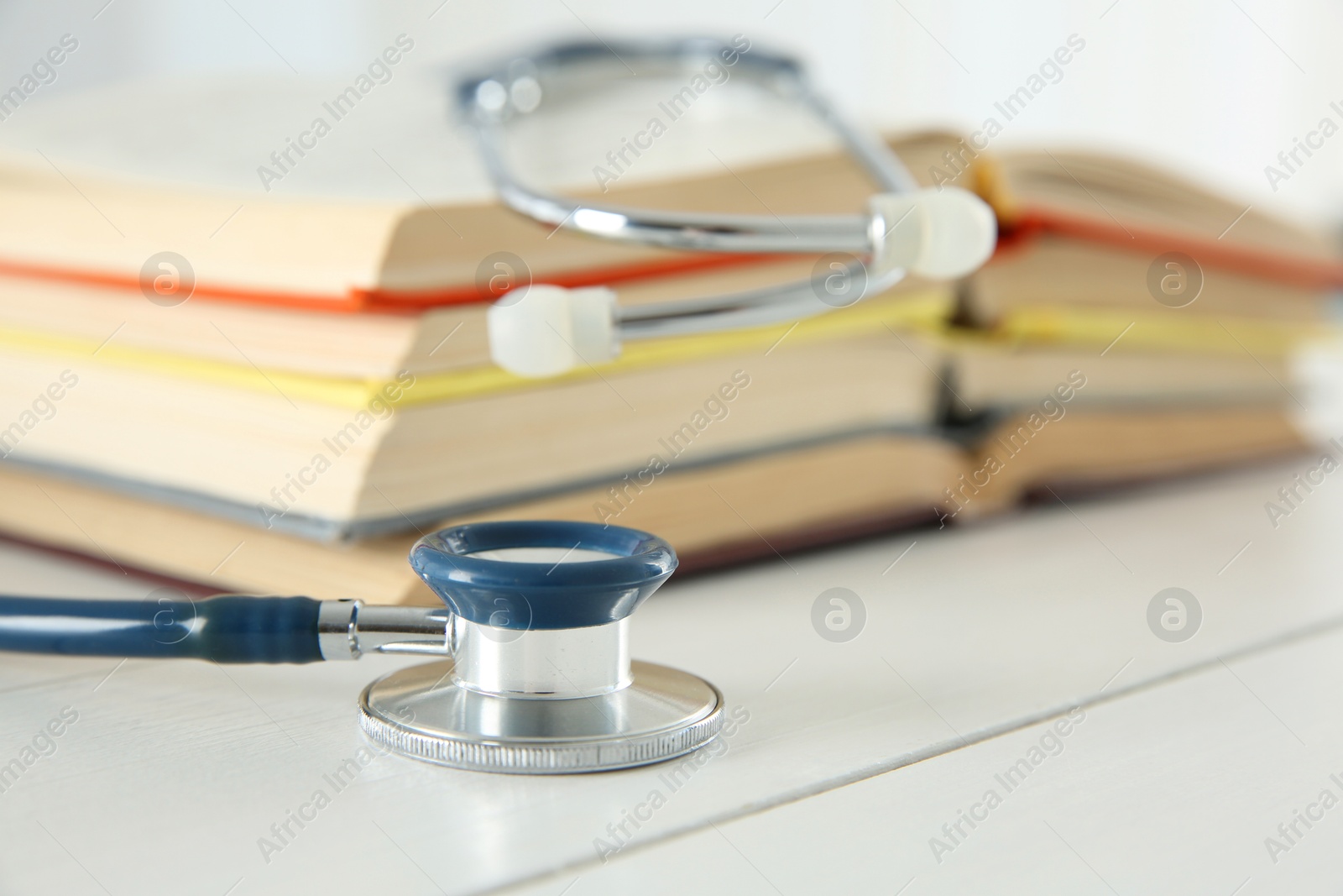 Photo of One new medical stethoscope and books on white wooden table, closeup