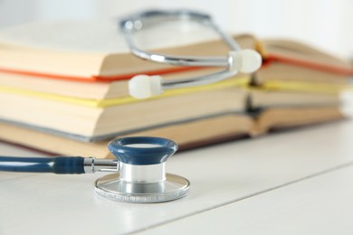 One new medical stethoscope and books on white wooden table, closeup