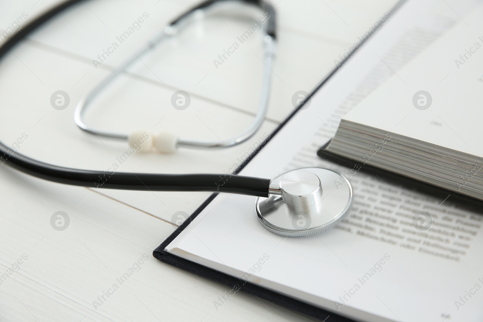 Photo of One new medical stethoscope and books on white wooden table, closeup