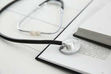 One new medical stethoscope and books on white wooden table, closeup