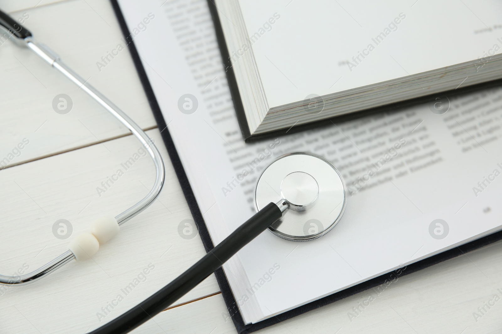 Photo of One new medical stethoscope and books on white wooden table, closeup