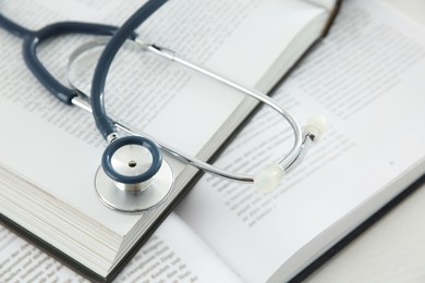 Photo of One new medical stethoscope and books on white wooden table