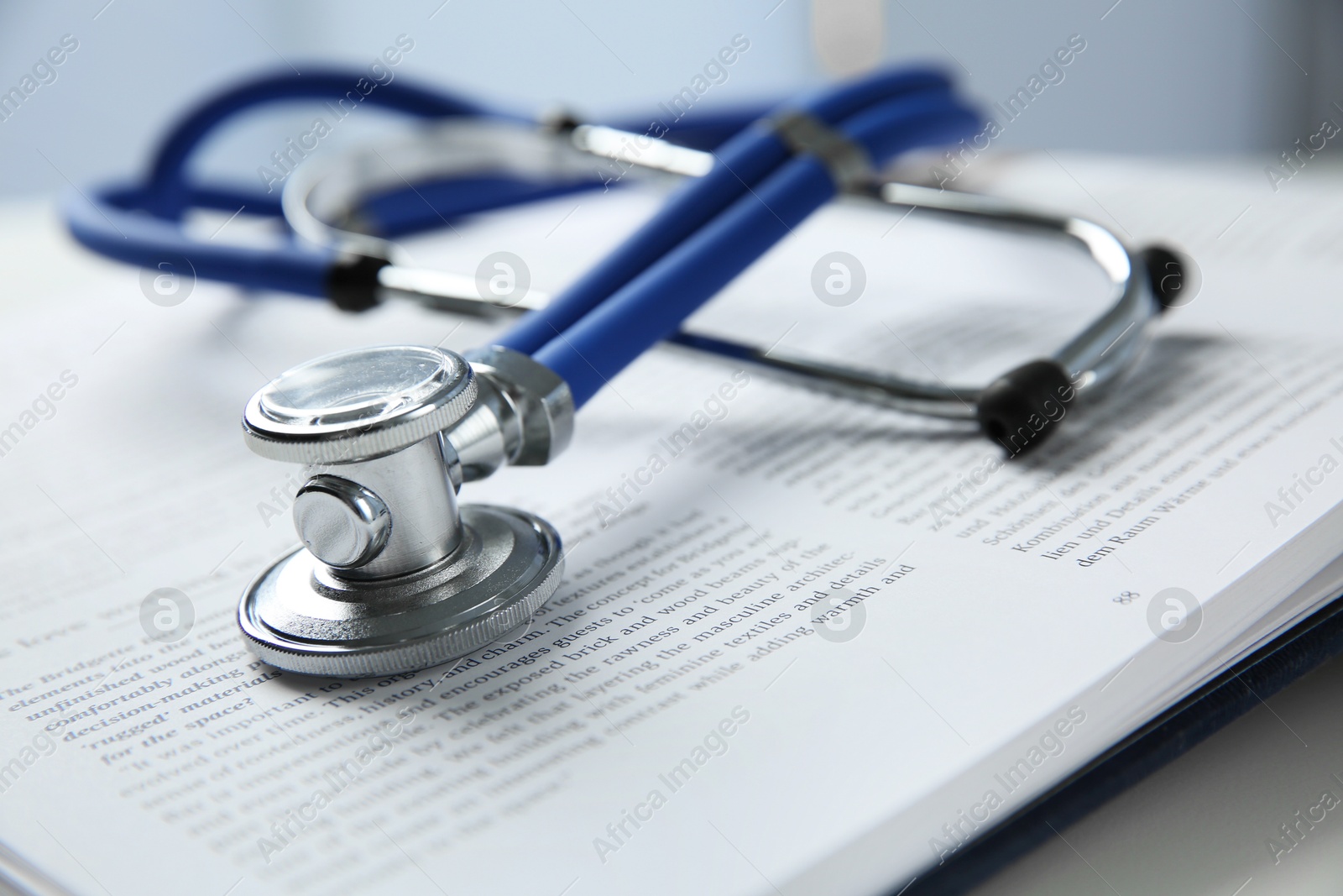 Photo of One medical stethoscope and book on white table, closeup