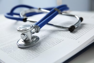 One medical stethoscope and book on white table, closeup