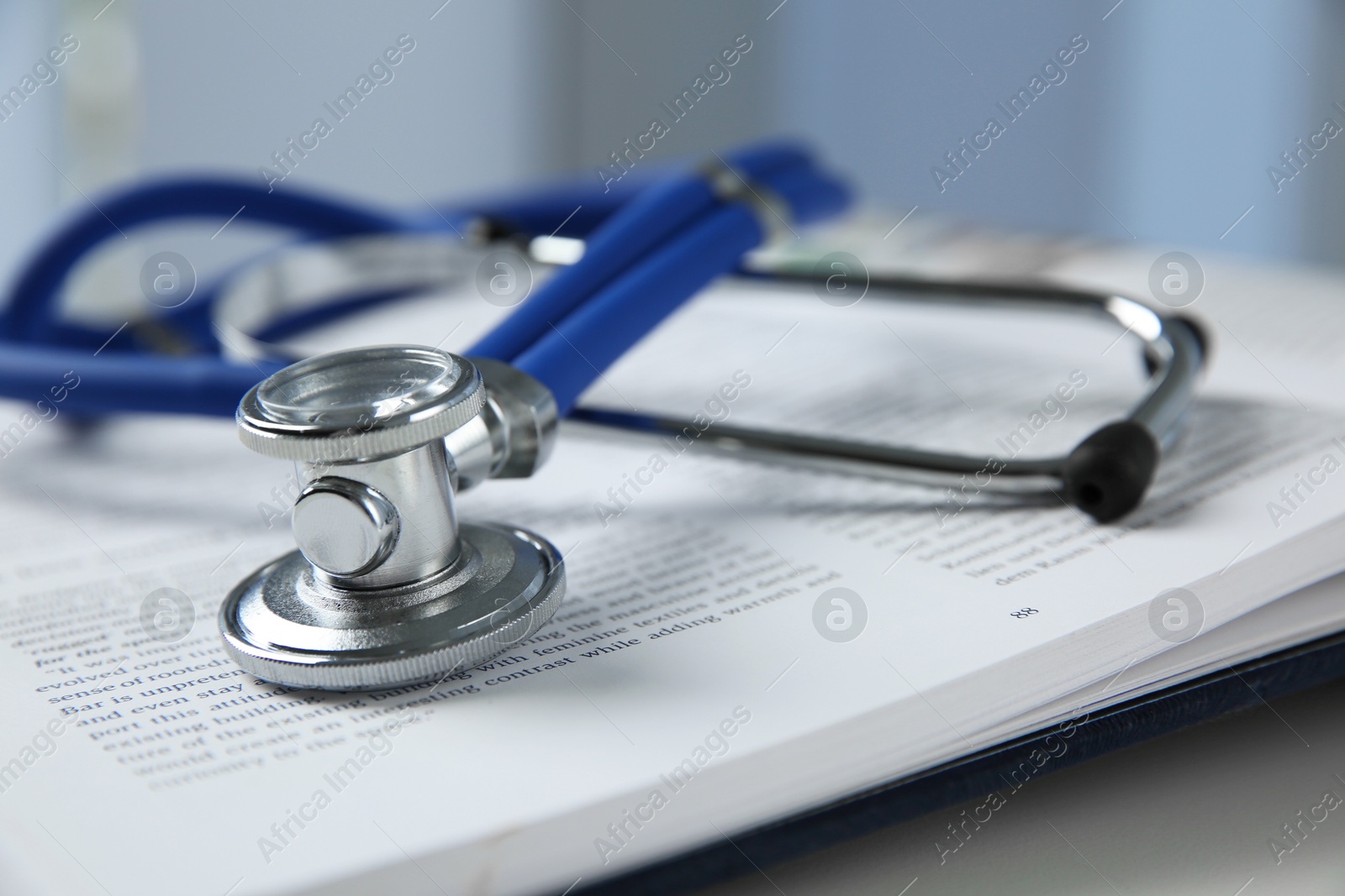 Photo of One medical stethoscope and book on white table, closeup