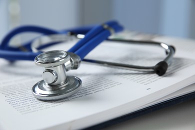 One medical stethoscope and book on white table, closeup