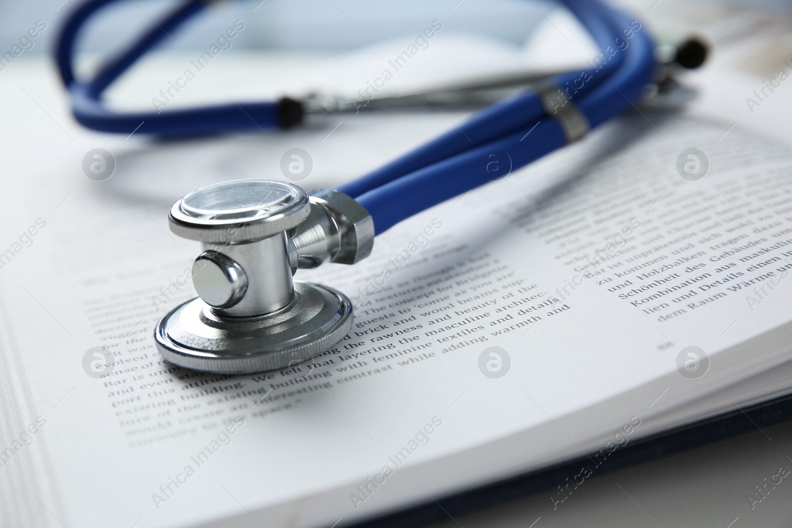 Photo of One medical stethoscope and book on white table, closeup