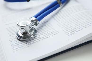 One medical stethoscope and book on white table, closeup