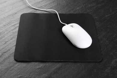 Photo of White wired mouse and mousepad on black textured table