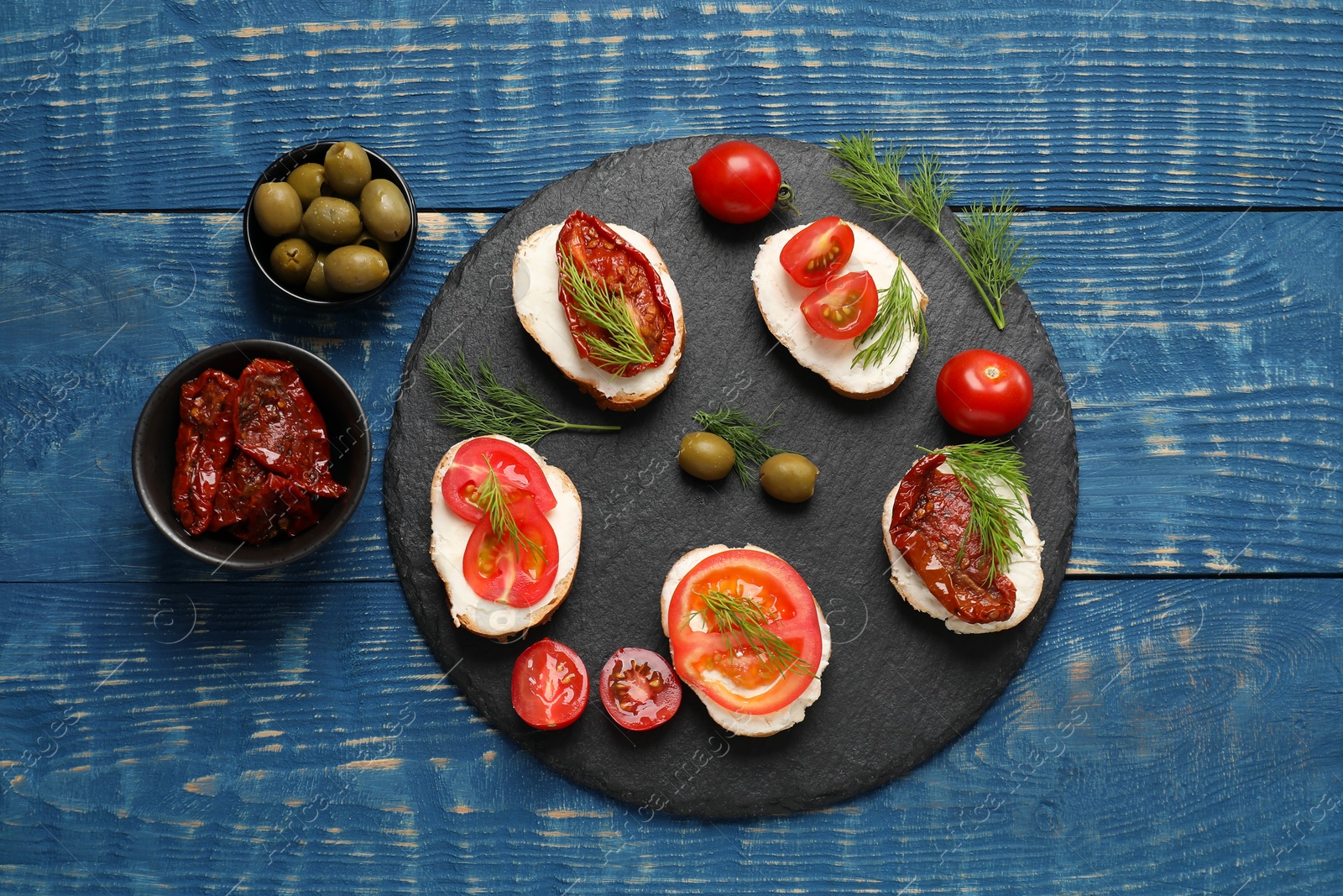 Photo of Delicious bruschettas with ricotta cheese, tomatoes, dill and olives on blue wooden table, flat lay