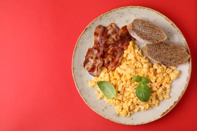 Photo of Delicious scrambled eggs with bacon and basil in plate on red background, top view. Space for text