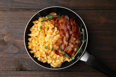 Photo of Delicious scrambled eggs with bacon in frying pan on wooden table, top view