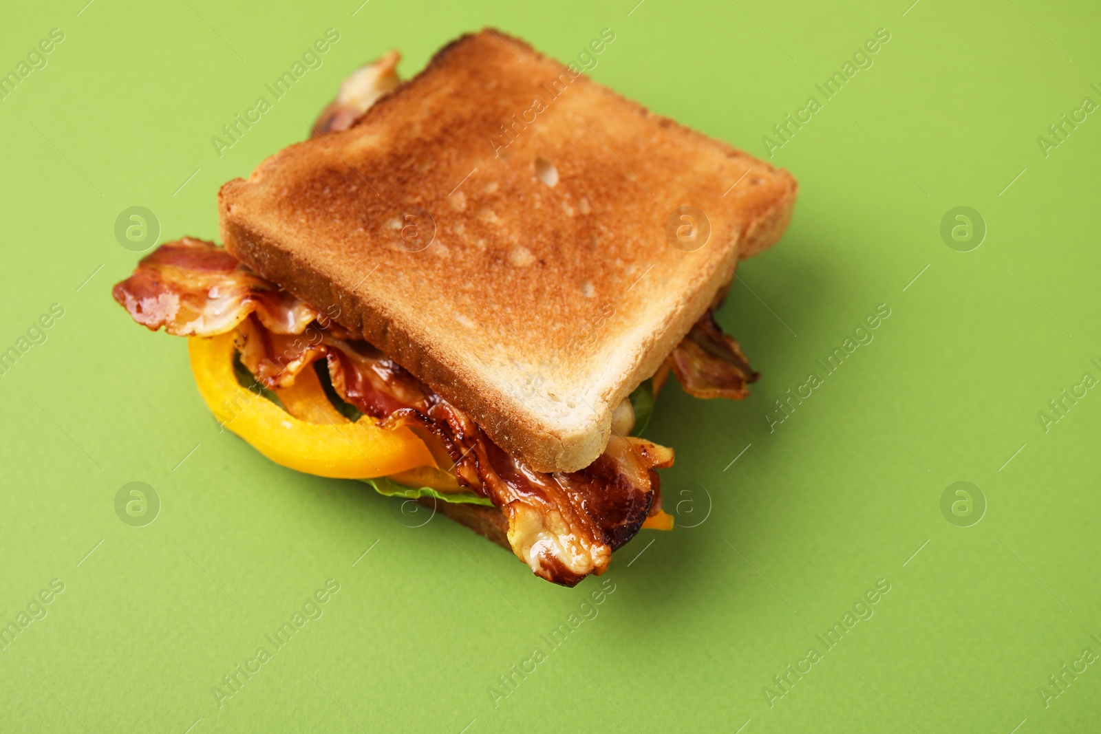 Photo of Tasty sandwich with bacon and bell pepper on green table