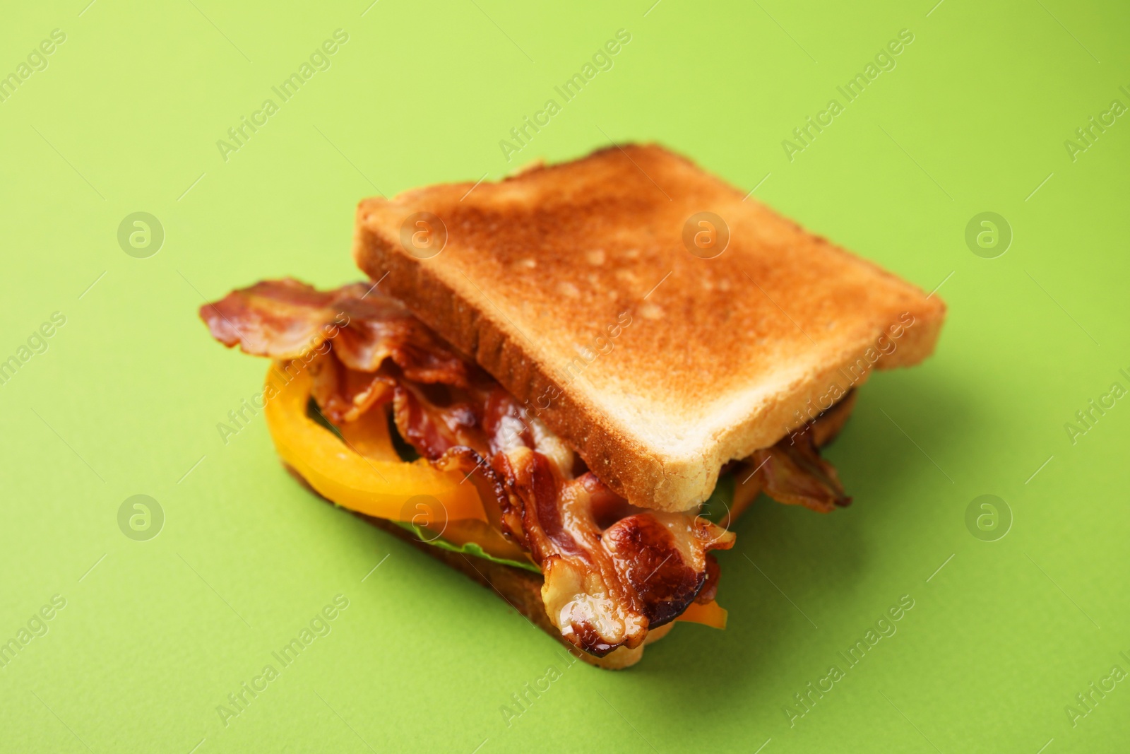 Photo of Tasty sandwich with bacon and bell pepper on green table