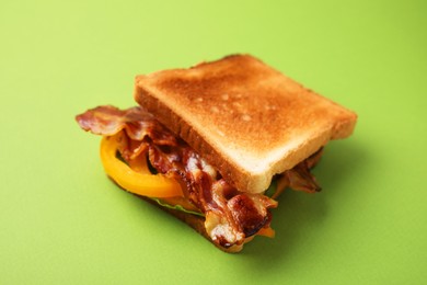 Photo of Tasty sandwich with bacon and bell pepper on green table