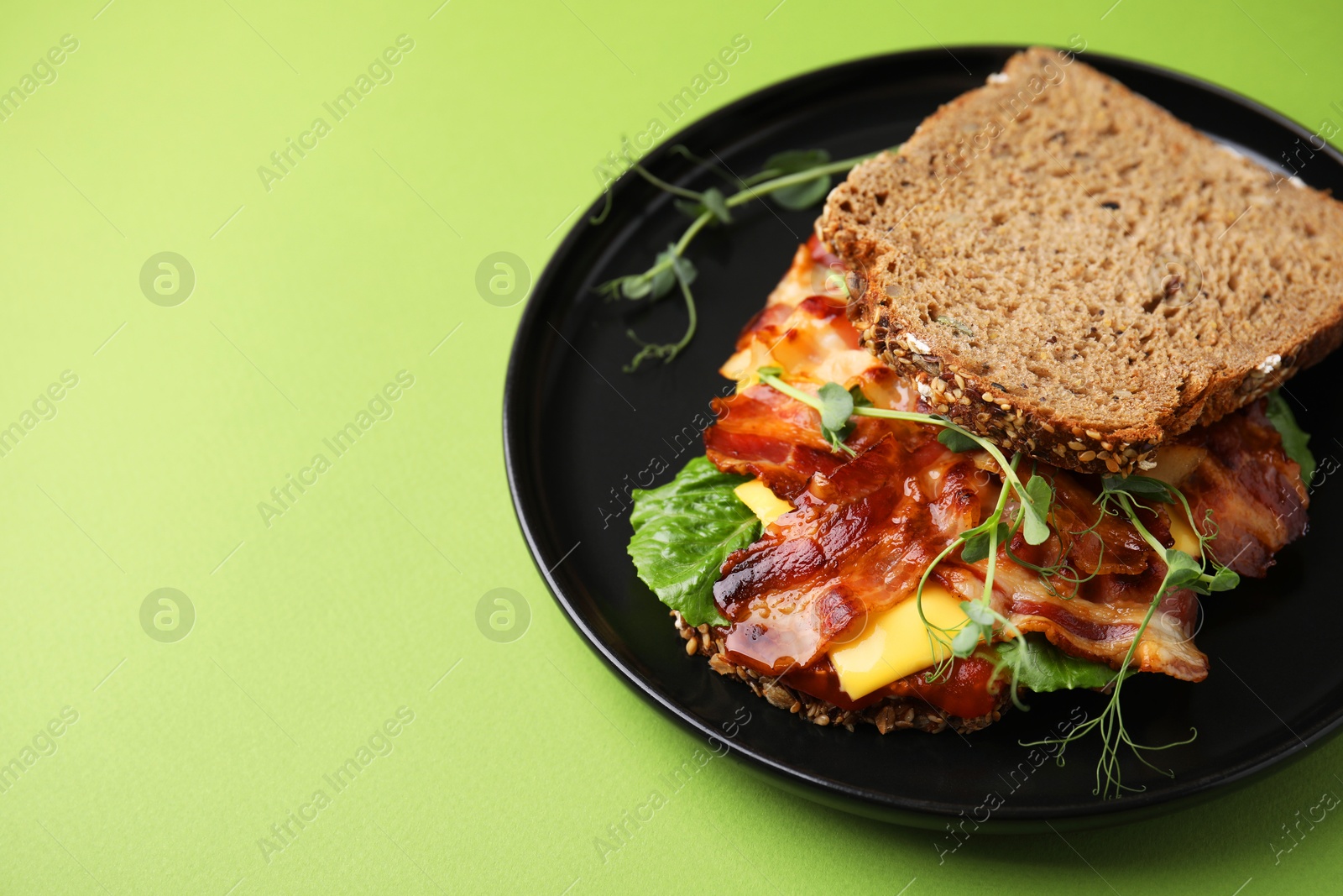 Photo of Tasty sandwich with bacon and microgreens on green table, space for text